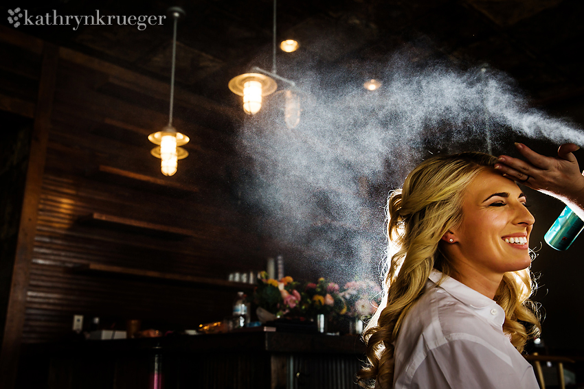 Bride smiling while getting hair sprayed. 