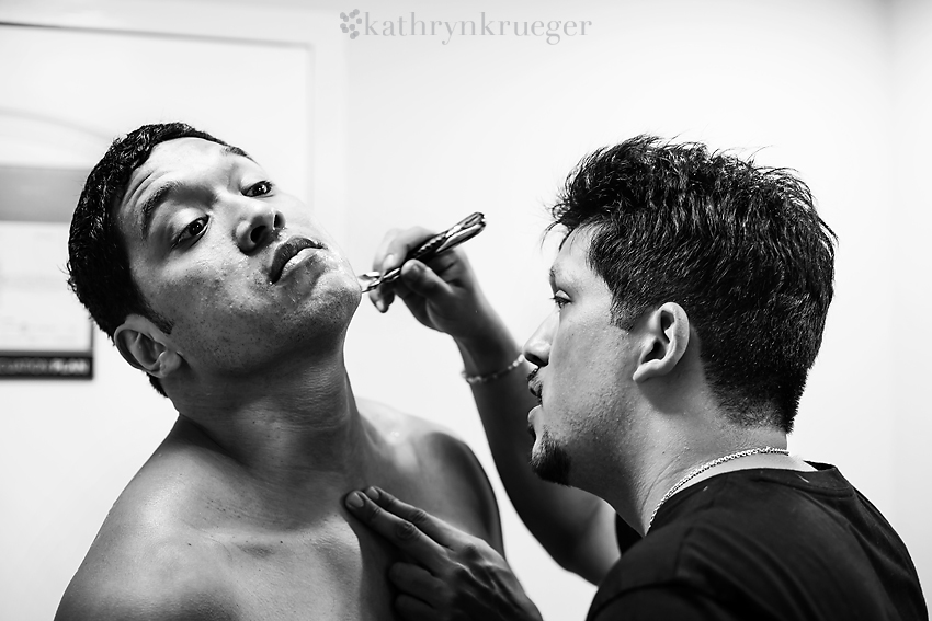 Groomsman helping groom shave neck in black and white.