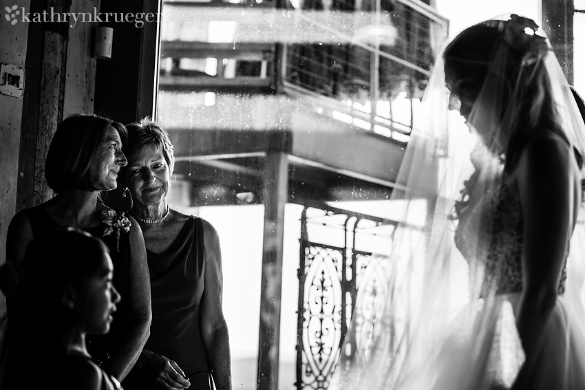 Black and white of mother of bride and groom look at bride in dress.