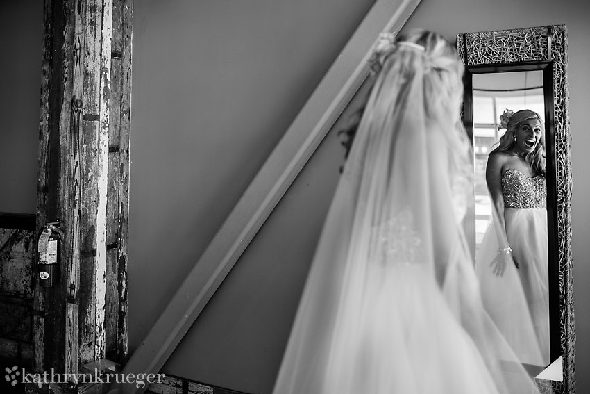 Excited bride looking at herself in the mirror in black and white.