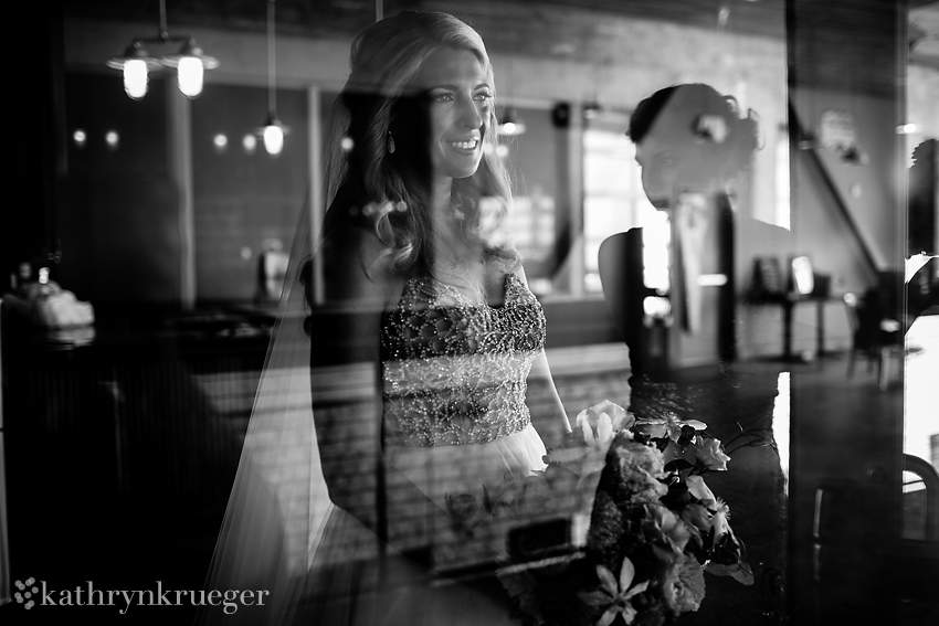 Black and white of bride smiling in window reflection.