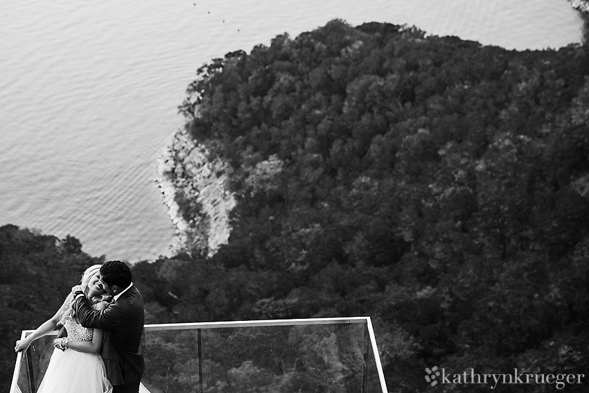 Black and white of bride and groom embracing on ledge over Lake Travis in Austin, Texas.