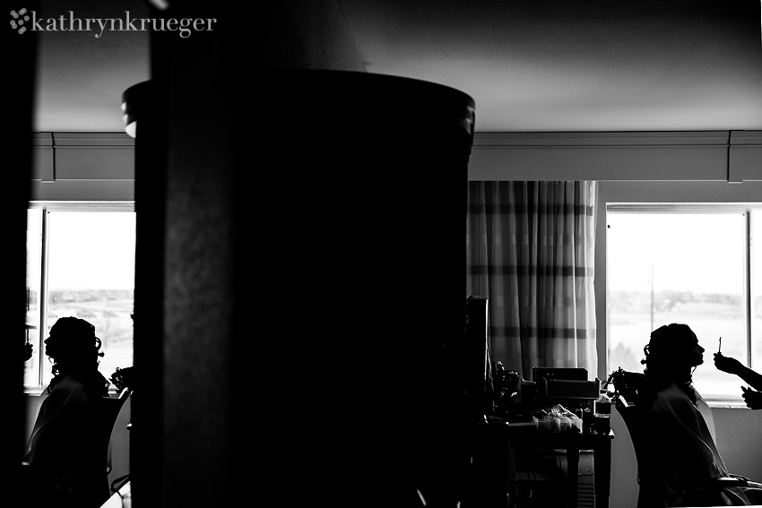 Black and white image of bride getting makeup done in hotel room.