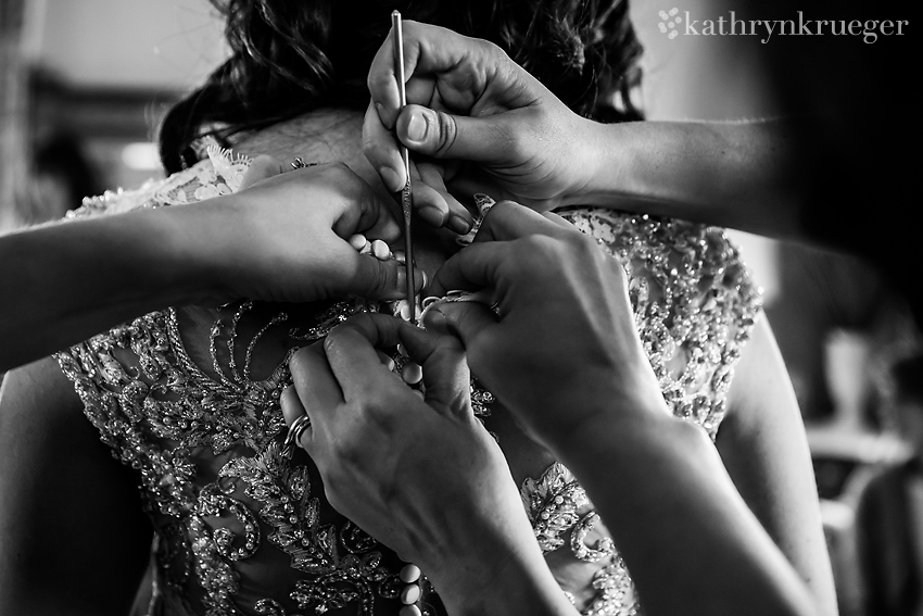 Black and white image of hands buttoning the brides dress.