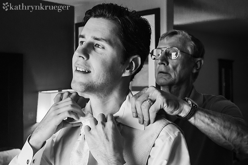 Black and white of groom getting help from his dad on his tie and collar.