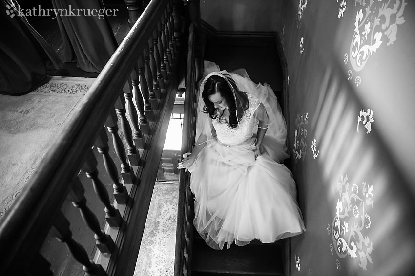 Black and white image of bride making her way downstairs to the ceremony space.