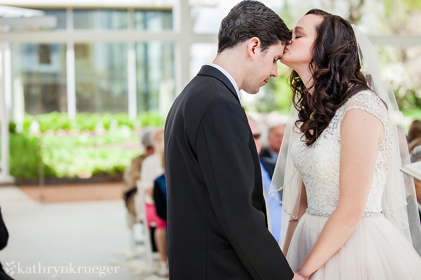 Bride kissing her groom on the forehead at altar.