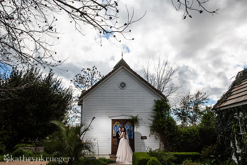 Bride and groom embracing in front of small chapel.