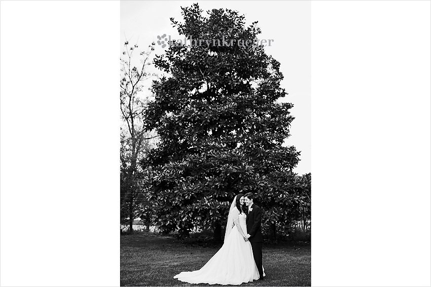 Black and white image of bride and groom holding hands in front of a magnolia tree.