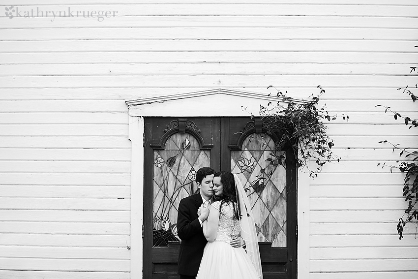 Black and white image of bride and groom close up in front of glass doors.