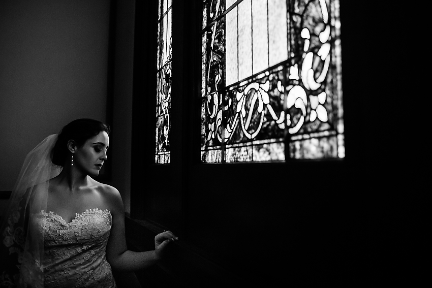 Black and white photo of a bride by a stained glass window