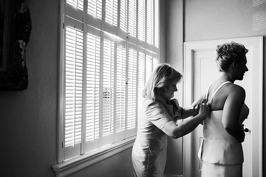 Black and white image of mother helping bride put on her dress.