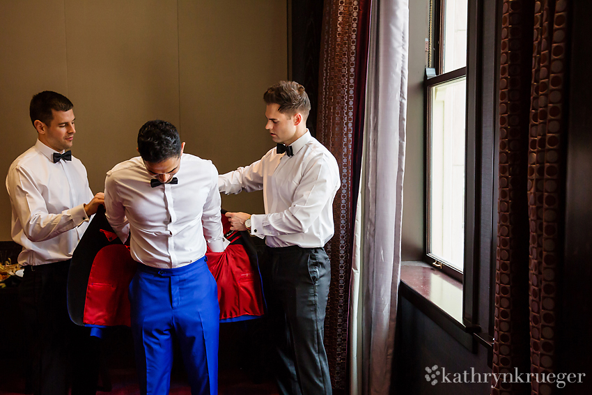 Groom putting on blue tuxedo jacket