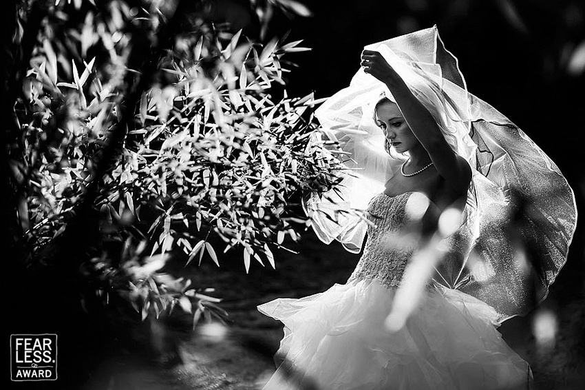 Black and white of bride pulling veil back by tree.